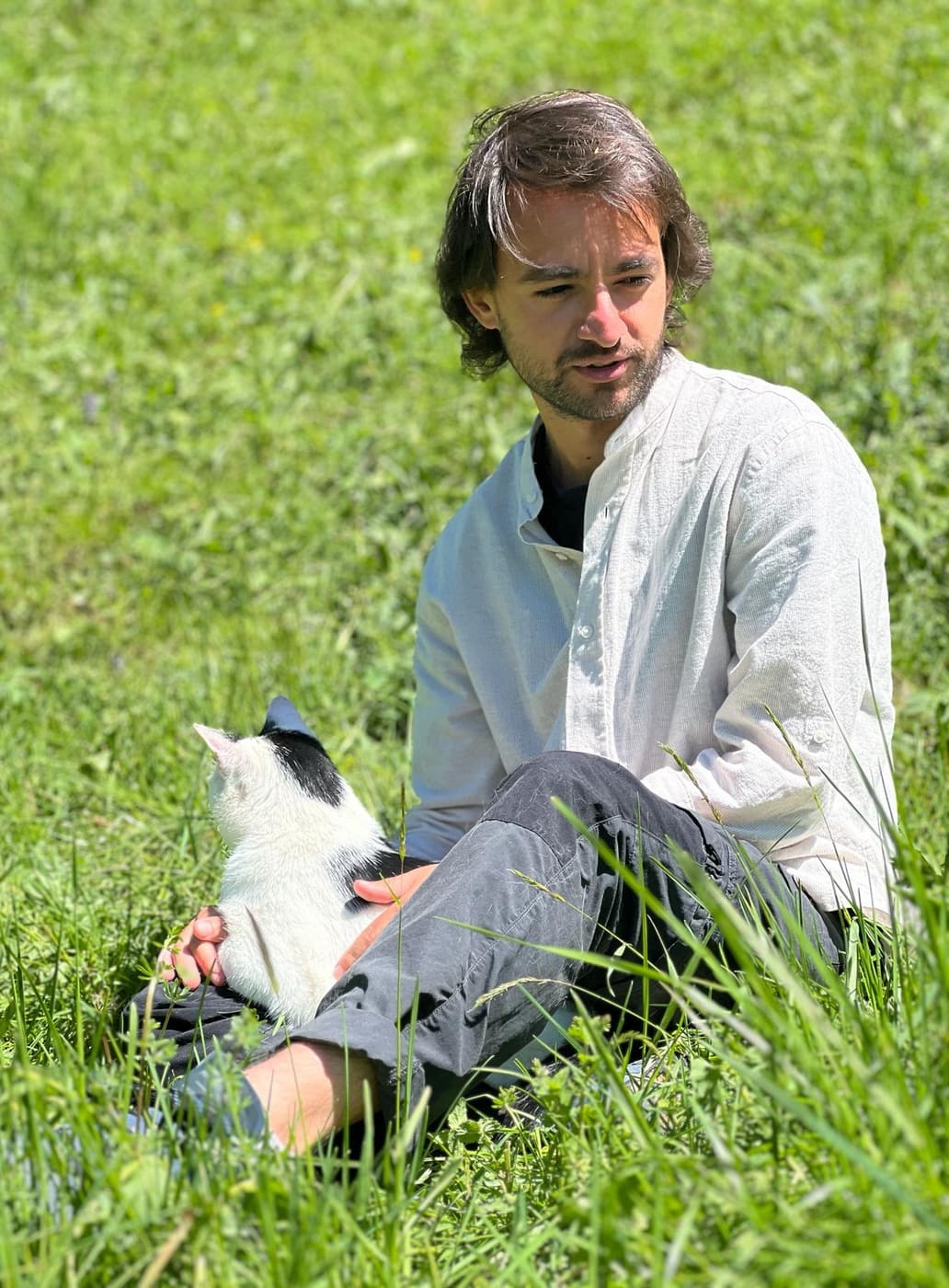 Kevin seduto su un prato, con un gatto in braccio